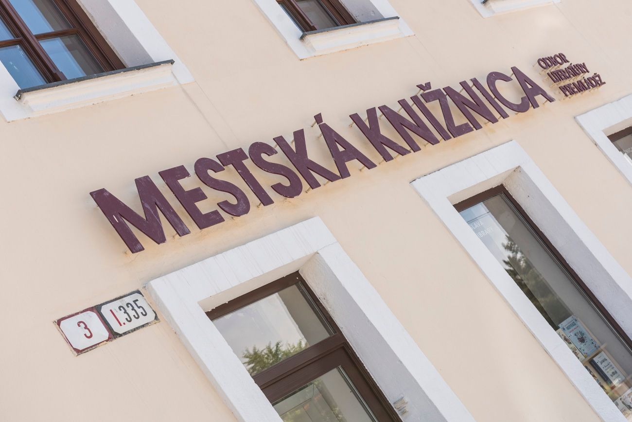 Popis fotografie: Na stene budovy nad oknami je nápis Mestská knižnica odbor literatúry pre deti a mládež. Vedľa okna je zavesené súpisné a opisné číslo budovy.